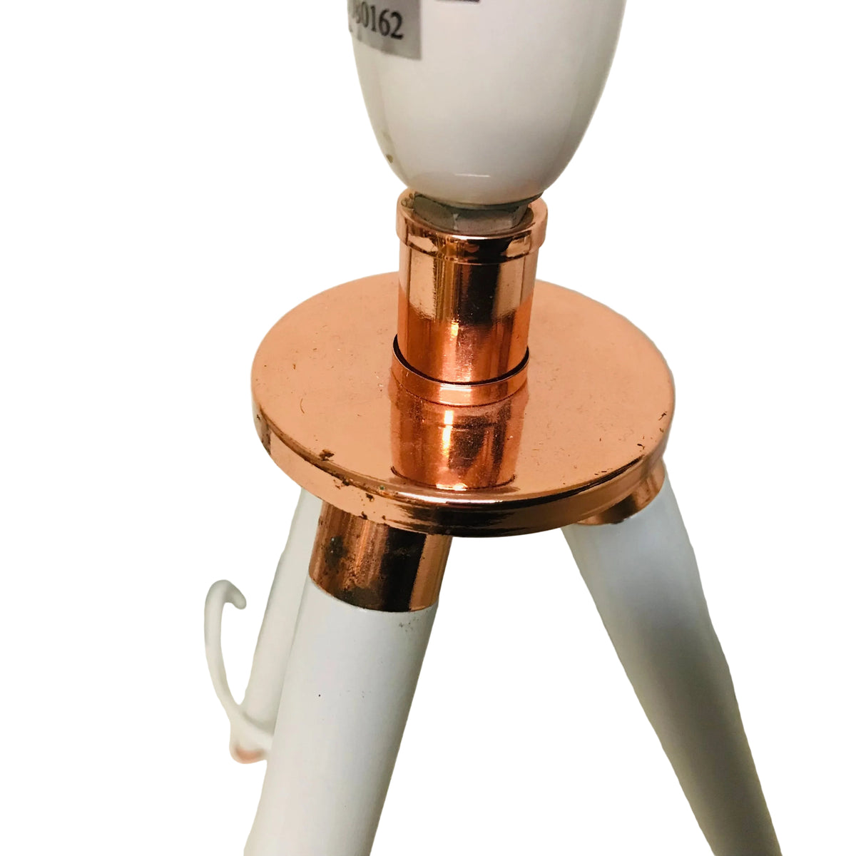 A close-up of a table lamp with a white tripod base and shiny copper-colored metal accents, showing a white bulb socket and part of a light bulb.