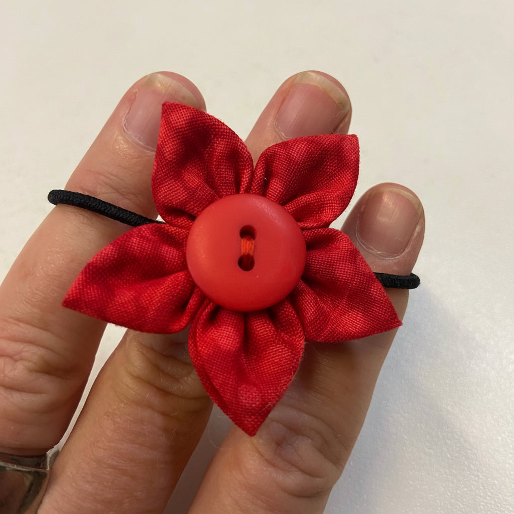Red fabric flower with a button center held between fingers on a light background