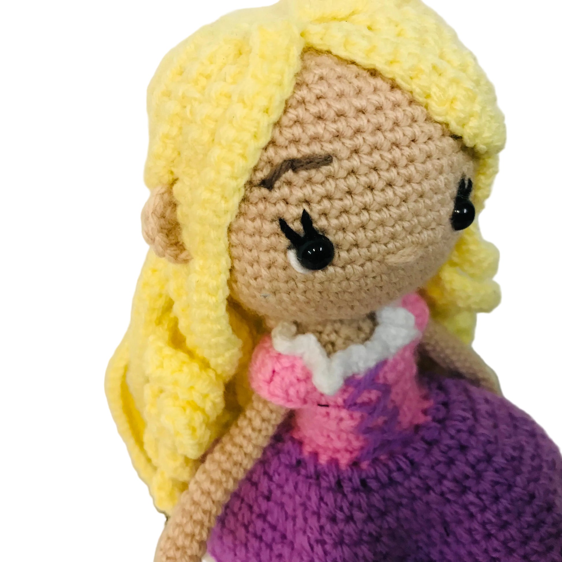 Crocheted doll with blonde hair, brown eyes, and a purple dress on a light background
