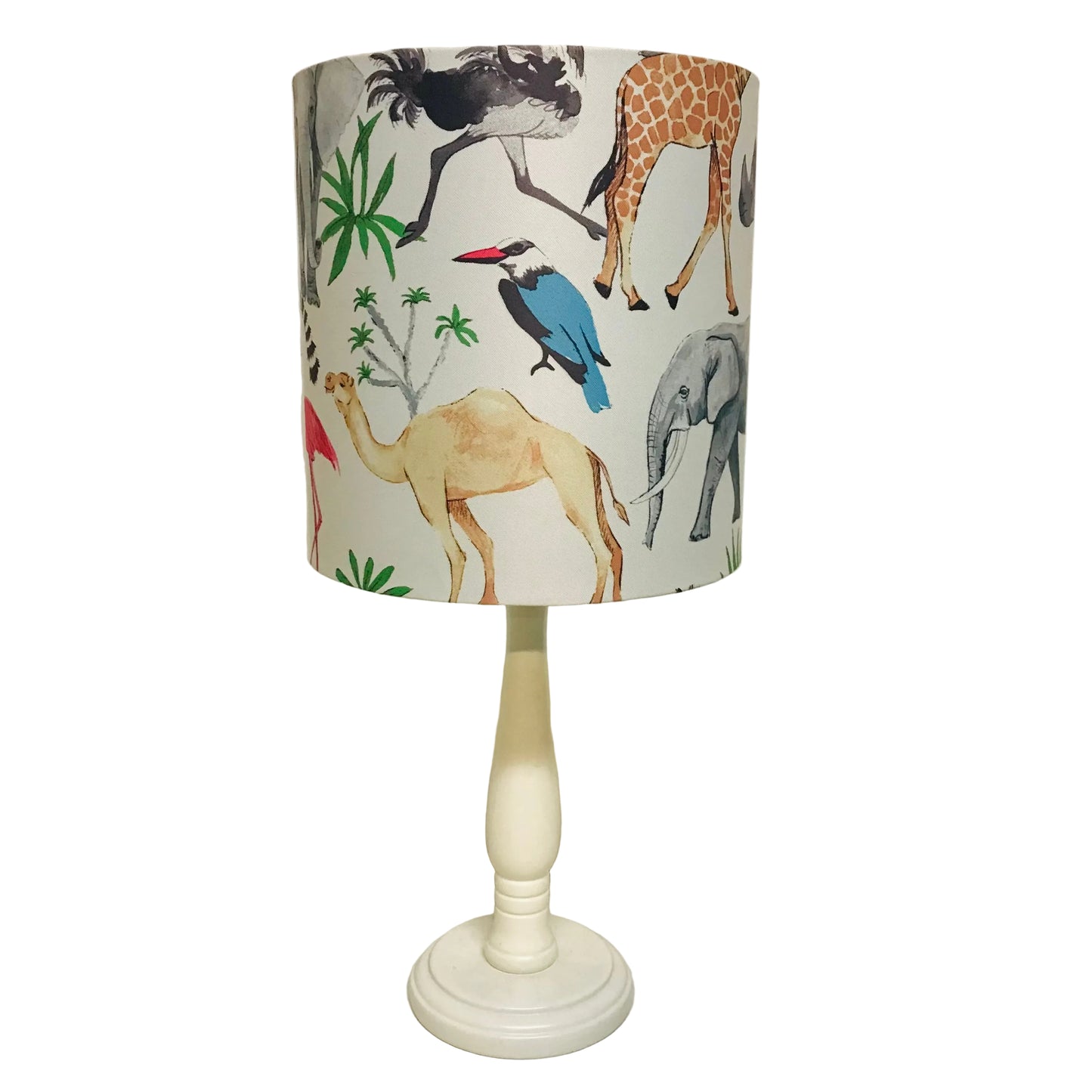 A table lamp with a cream-colored turned wood pedestal base and a cylindrical fabric shade featuring a colorful safari animal print with a giraffe, elephant, camel, bird, and palm trees on a light background.