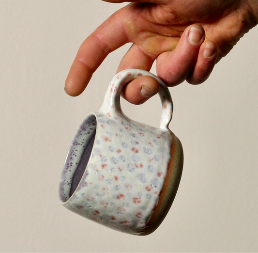 Hand holding a ceramic mug with floral pattern against a neutral background