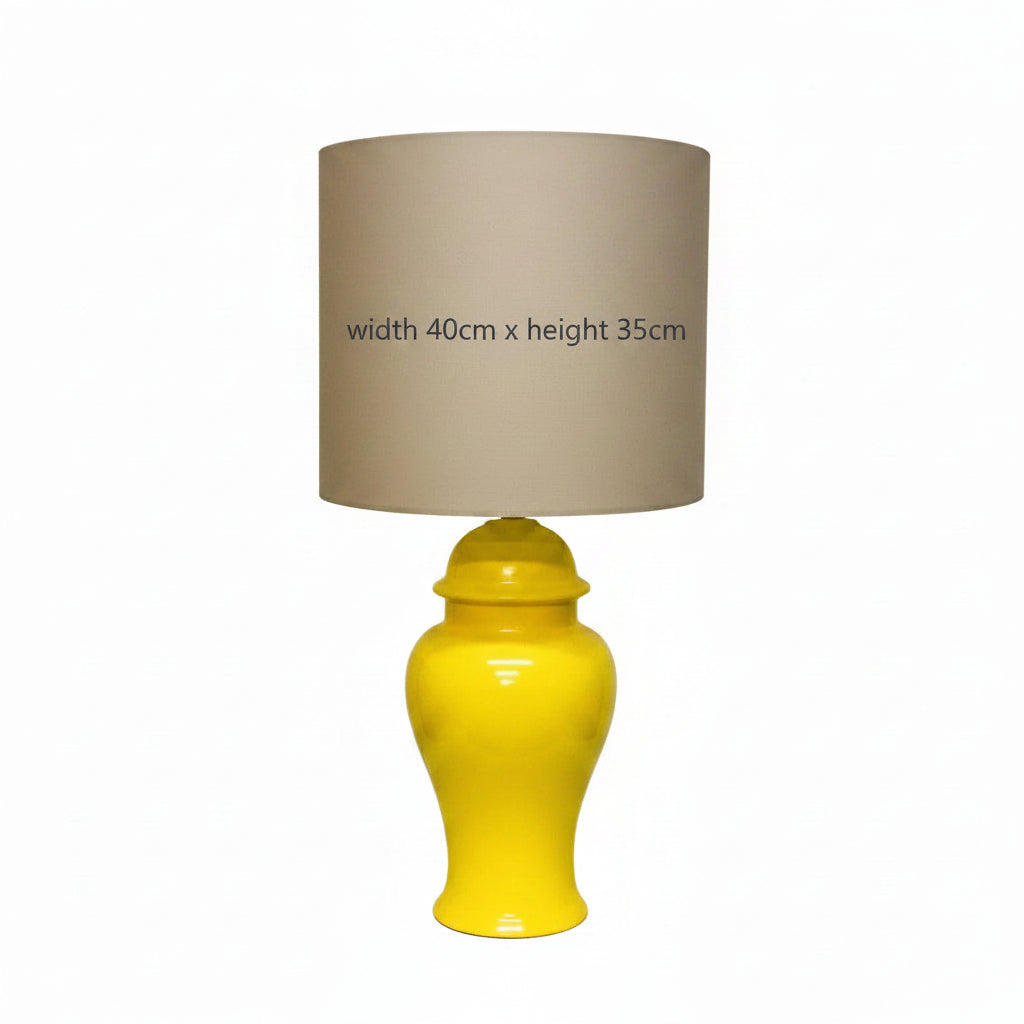A yellow ceramic table lamp with a brown fabric shade, featuring a white sample label on the shade that reads 'SAMPLE SHADE ONLY' with dimensions and customization details.