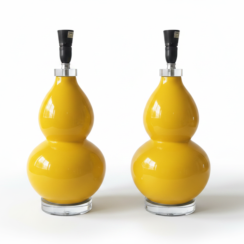Two matching glossy yellow gourd-shaped table lamps with black lamp fittings and clear round bases, photographed on a clean white studio background.