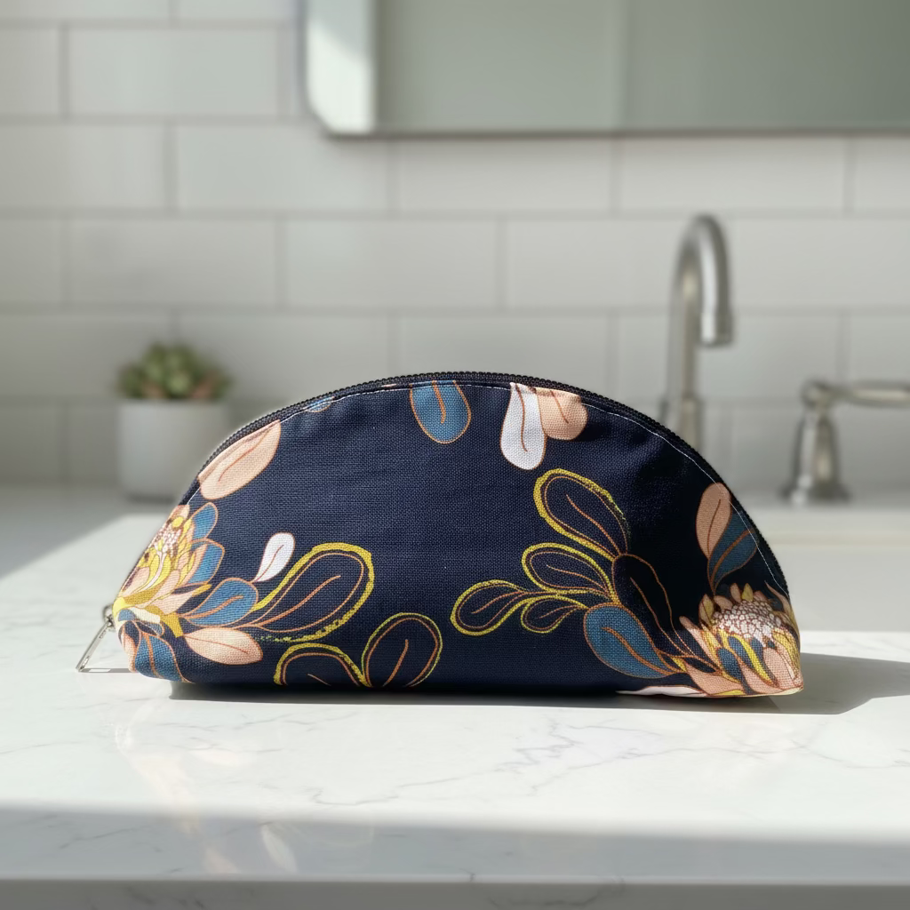 A navy blue zippered pouch with a floral and botanical pattern in pink, yellow, and blue, resting on a white surface with cardboard boxes in the background.