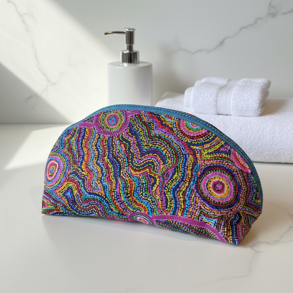 A zippered pouch with a vibrant multicolor beaded pattern inspired by Aboriginal dot art, featuring concentric circles and wavy lines in pink, blue, yellow, green, and purple, with a light blue zipper.