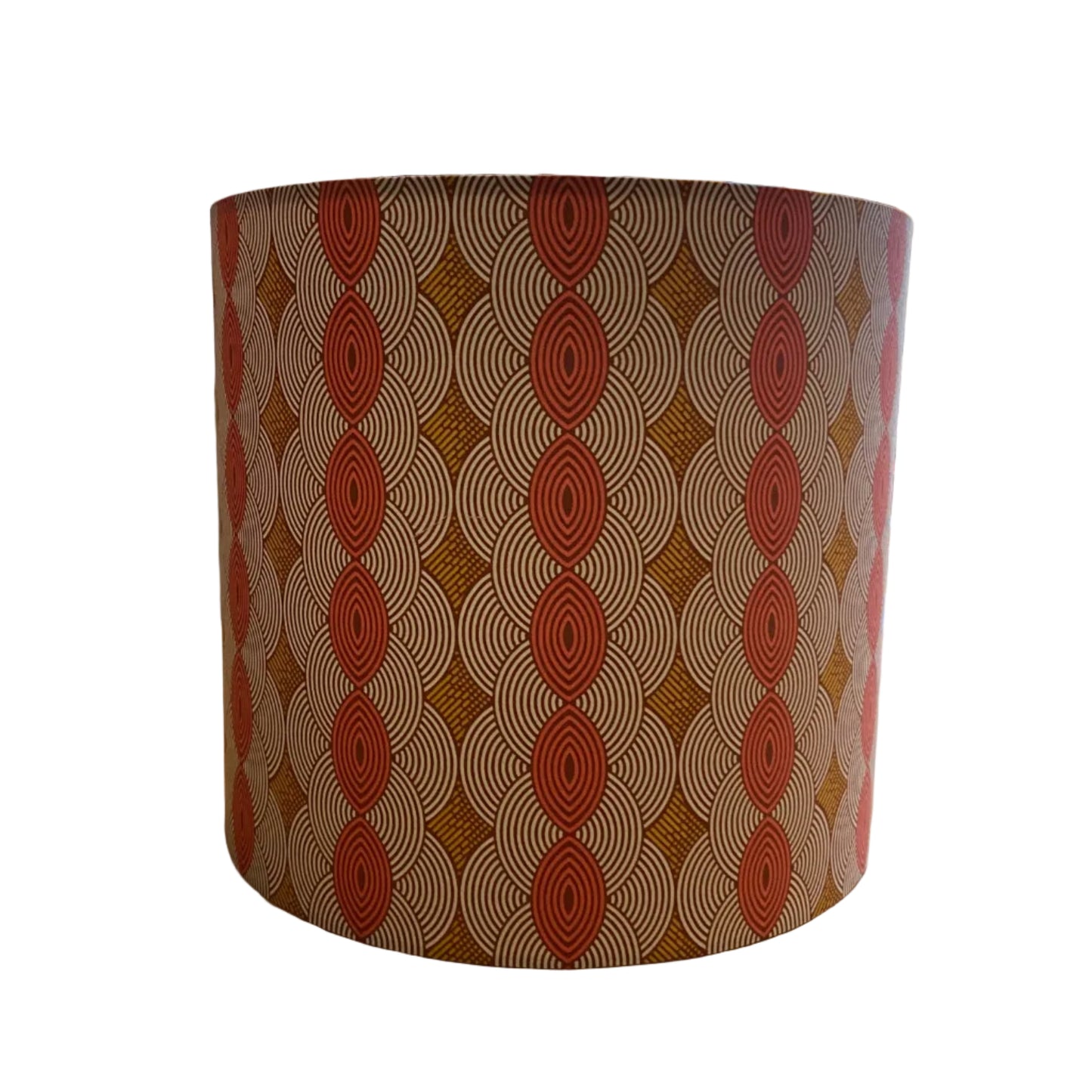 A cylindrical lampshade featuring a repeating geometric pattern of red-orange concentric ovals and diamond shapes over a warm brown and beige background, shown against a plain white background.
