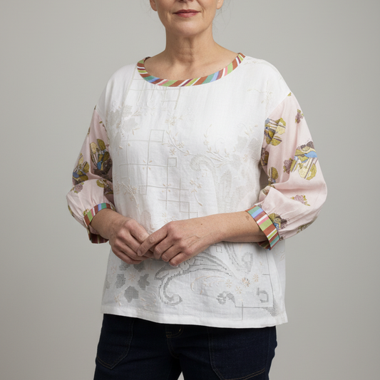 A woman wearing a white embroidered blouse with pastel pink sleeves featuring a floral print and striped trim