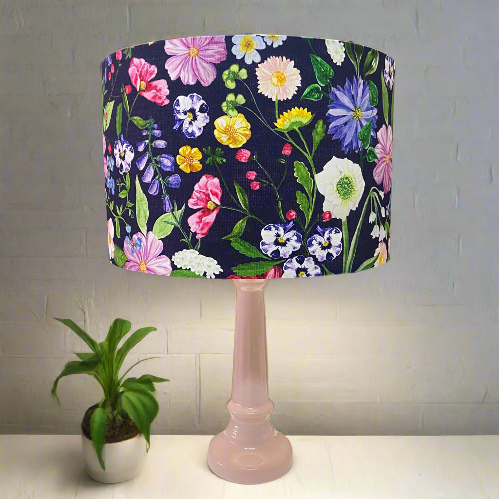 A pink ceramic table lamp with a floral lampshade, placed on a pink base, next to a small potted plant.