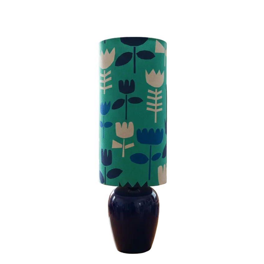 A table lamp with a drum shade featuring a retro floral pattern in navy and beige, mounted on a glossy dark blue ceramic base against a plain white background.
