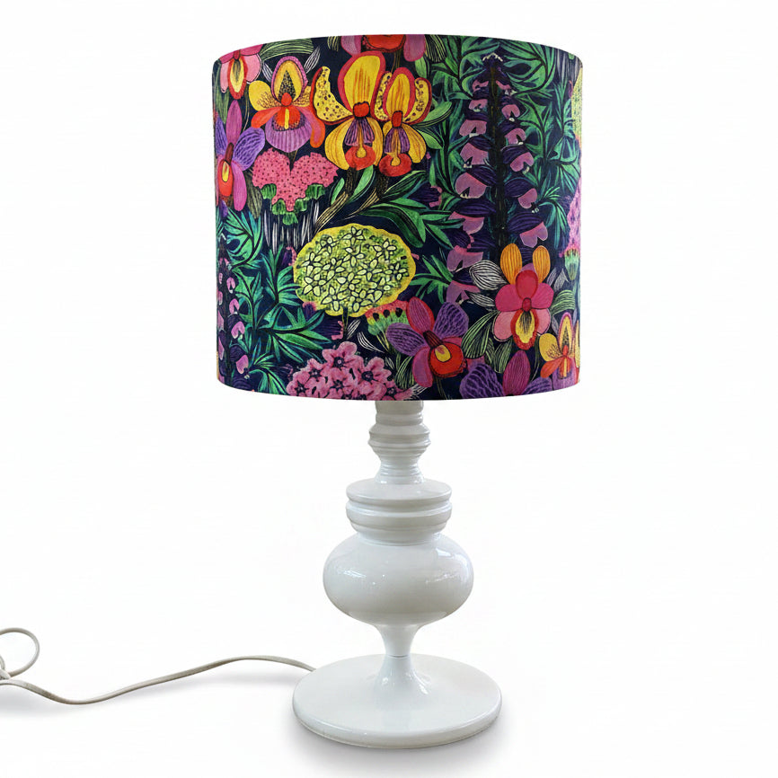 A white table lamp with a vibrant, multicolored floral and botanical patterned drum shade, set on a white background