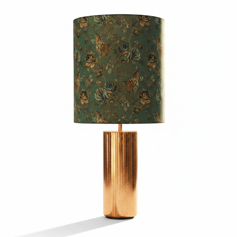 A table lamp with a cylindrical metallic gold base and a matching cylindrical shade featuring a vintage floral pattern in green, gold, and blue velvet set against a plain white background.