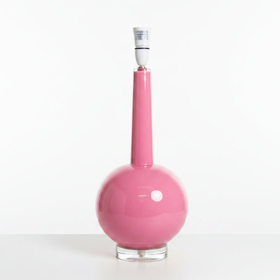 A modern pink table lamp with a glossy spherical base, a long narrow neck, and a clear glass or acrylic circular stand, shown on a white background.
