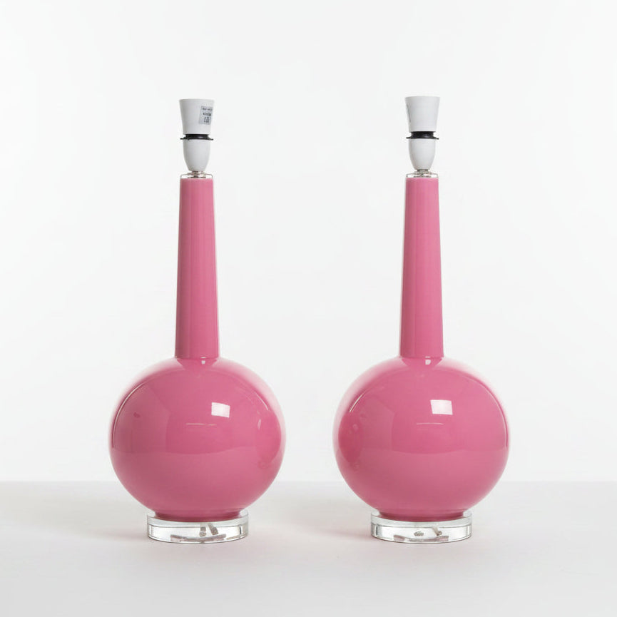 A pair of glossy pink ceramic table lamps with spherical bases, narrow necks, white stoppers, and clear glass bases, set against a plain white background.