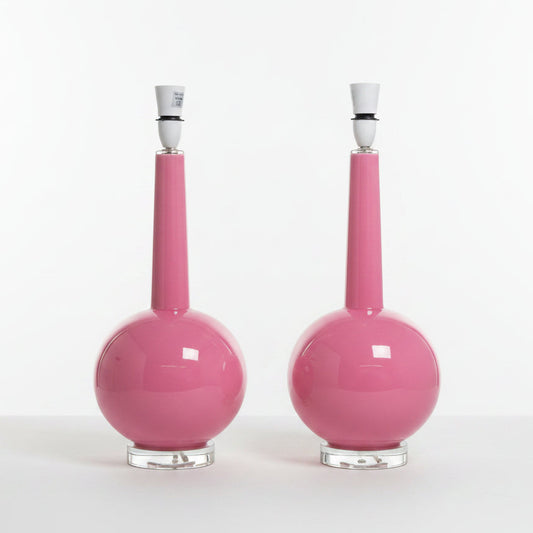 A pair of glossy pink ceramic table lamps with spherical bases, narrow necks, white stoppers, and clear glass bases, set against a plain white background.
