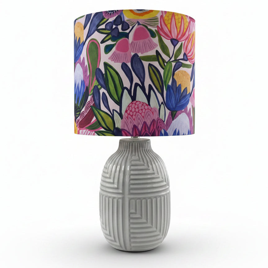 A table lamp with a textured white ceramic base and a vibrant floral patterned drum shade, displayed on a White background