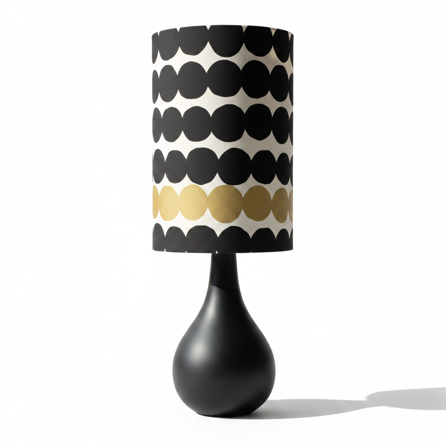 A modern table lamp with a glossy black teardrop-shaped base and a cylindrical drum shade featuring a black and cream scalloped pattern with a horizontal band of gold scallops, shown on a white background with a soft shadow.