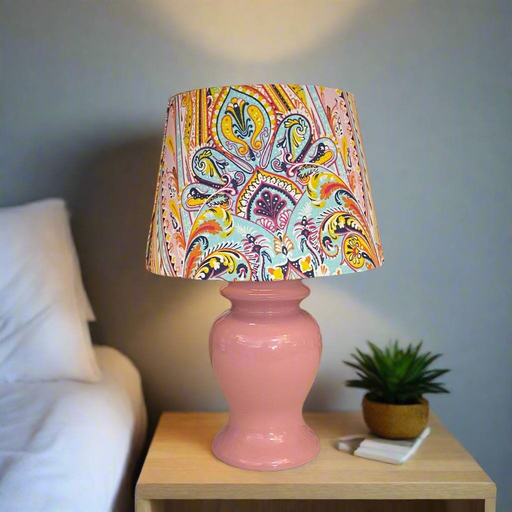 small mid century pink table lamp with a paisley empire shade sitting on a bedise table in a bedroom