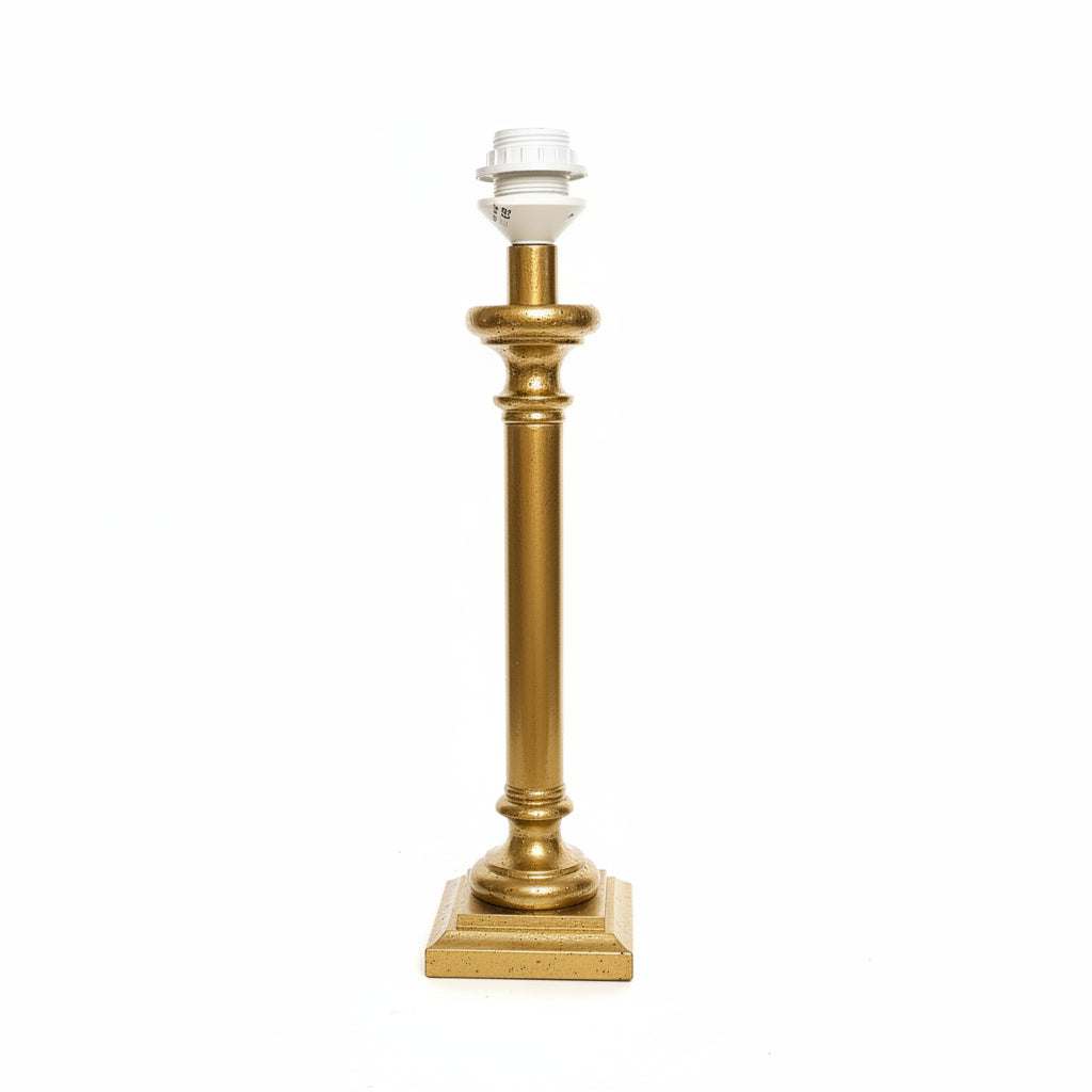 A vintage-style table lamp with a polished gold column base and a white cord, standing against a plain off-white wall.
