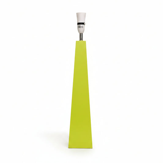 A modern geometric floor lamp with a bright lime green pyramid-shaped base, a silver metal stem, and a white ceramic bulb holder, shown standing on a light gray floor against a white wall.