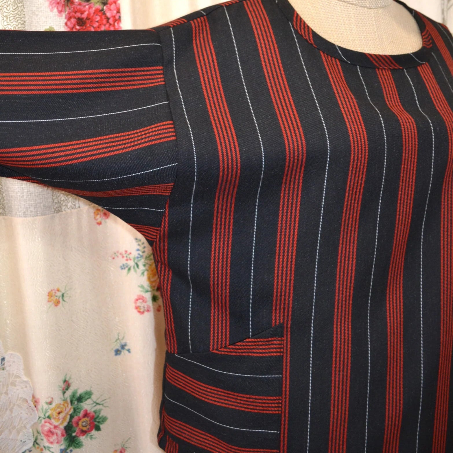 Black and red striped  long sleeved kite top on a mannequin against a floral curtain background