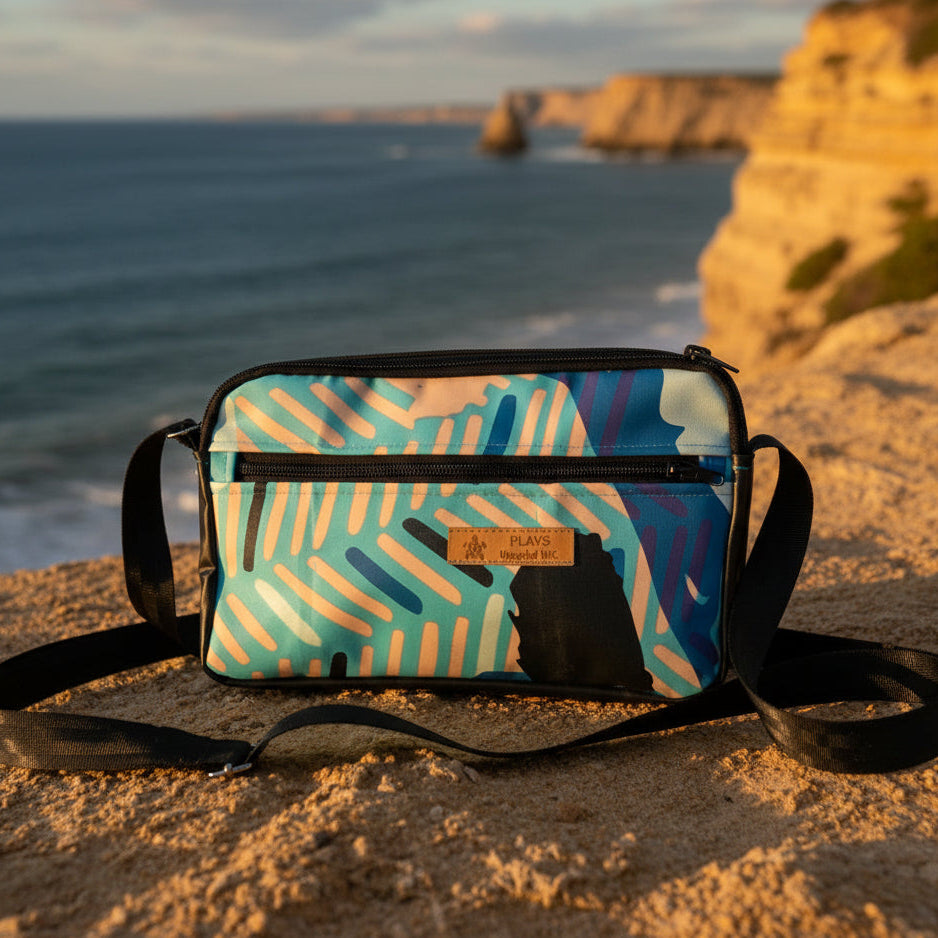 Colorful patterned bag on a sandy beach with ocean and cliffs in the background
