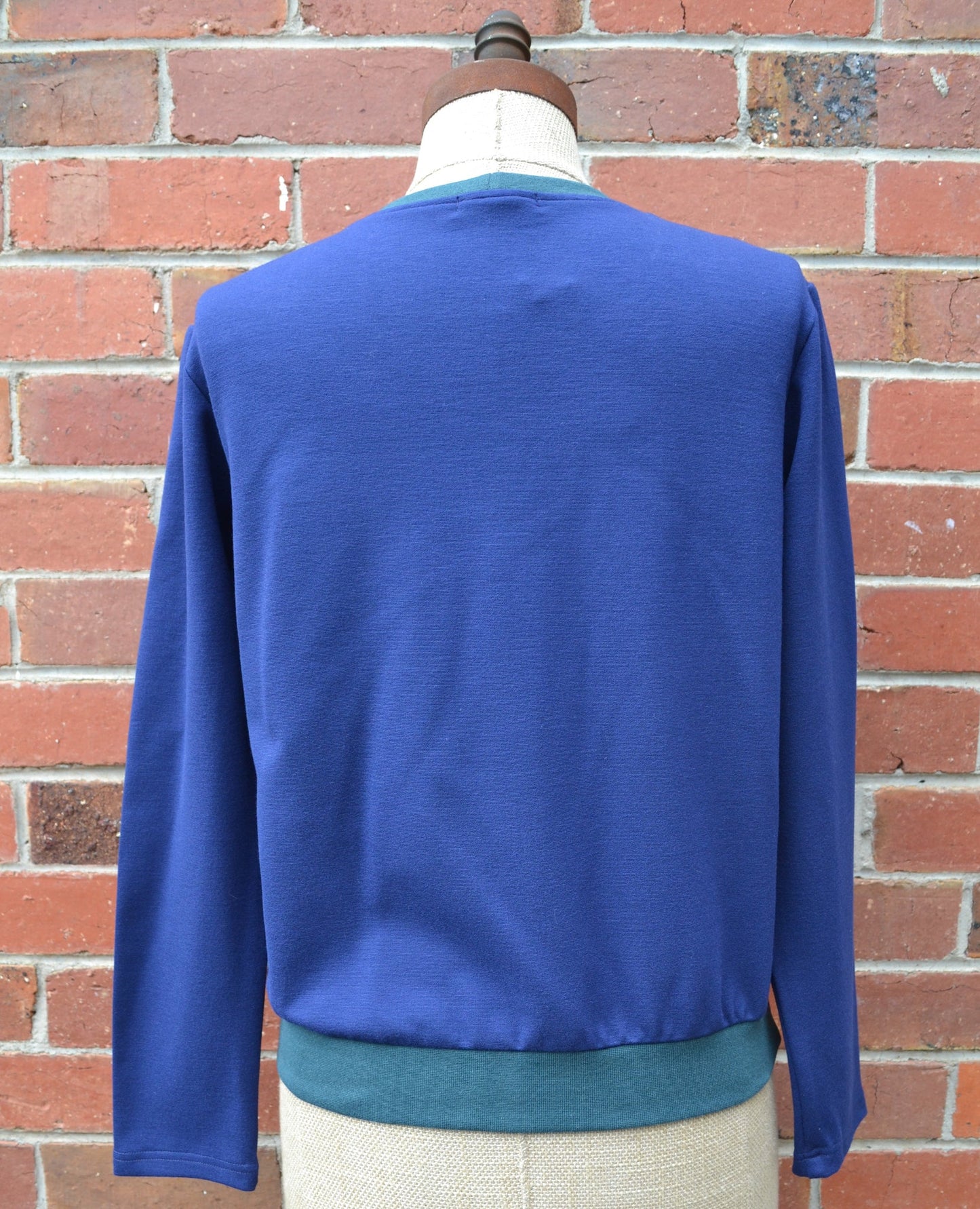Blue back of the patchwork long-sleeve sweater on a mannequin against a brick wall