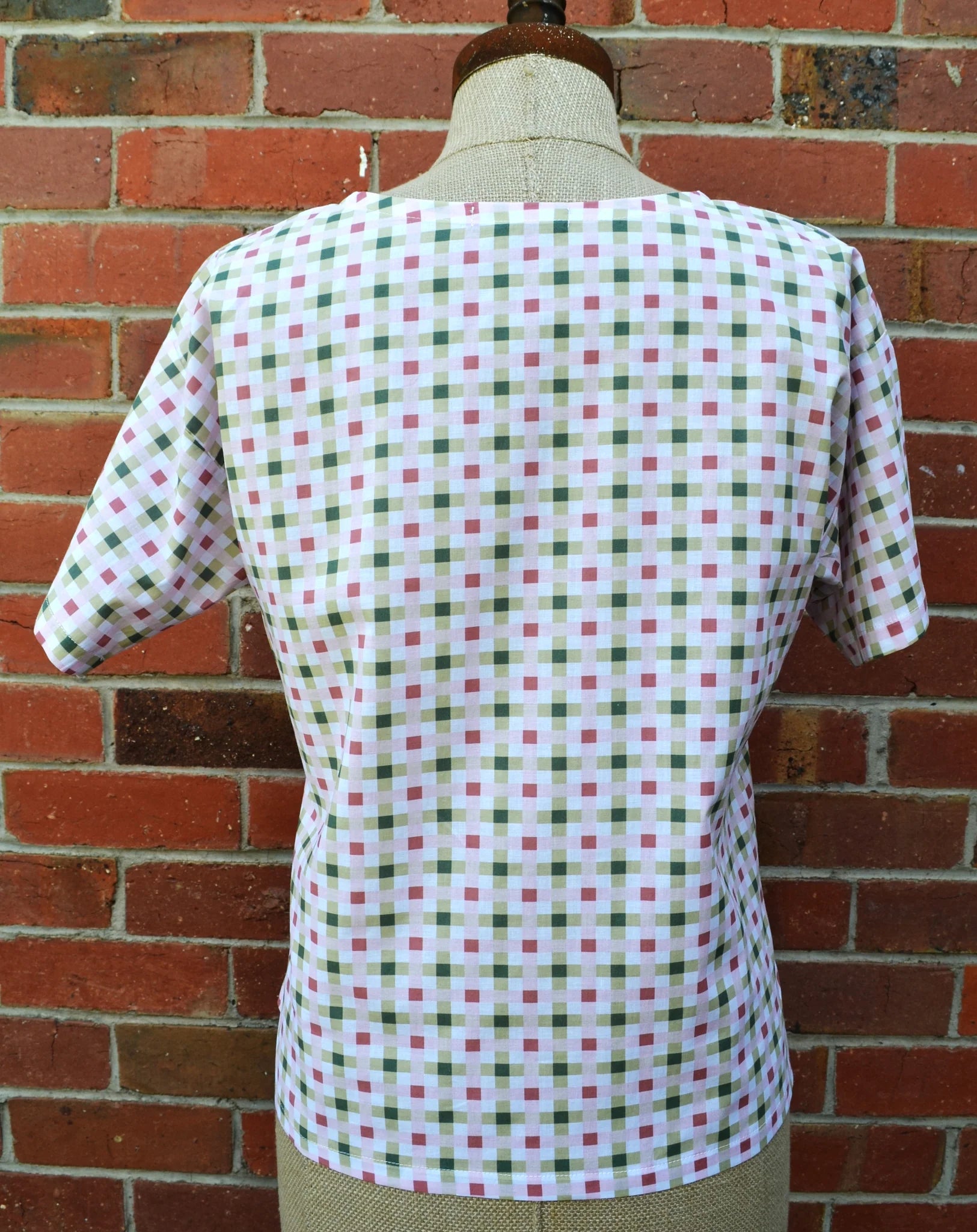 Mannequin wearing a checkered shirt against a brick wall