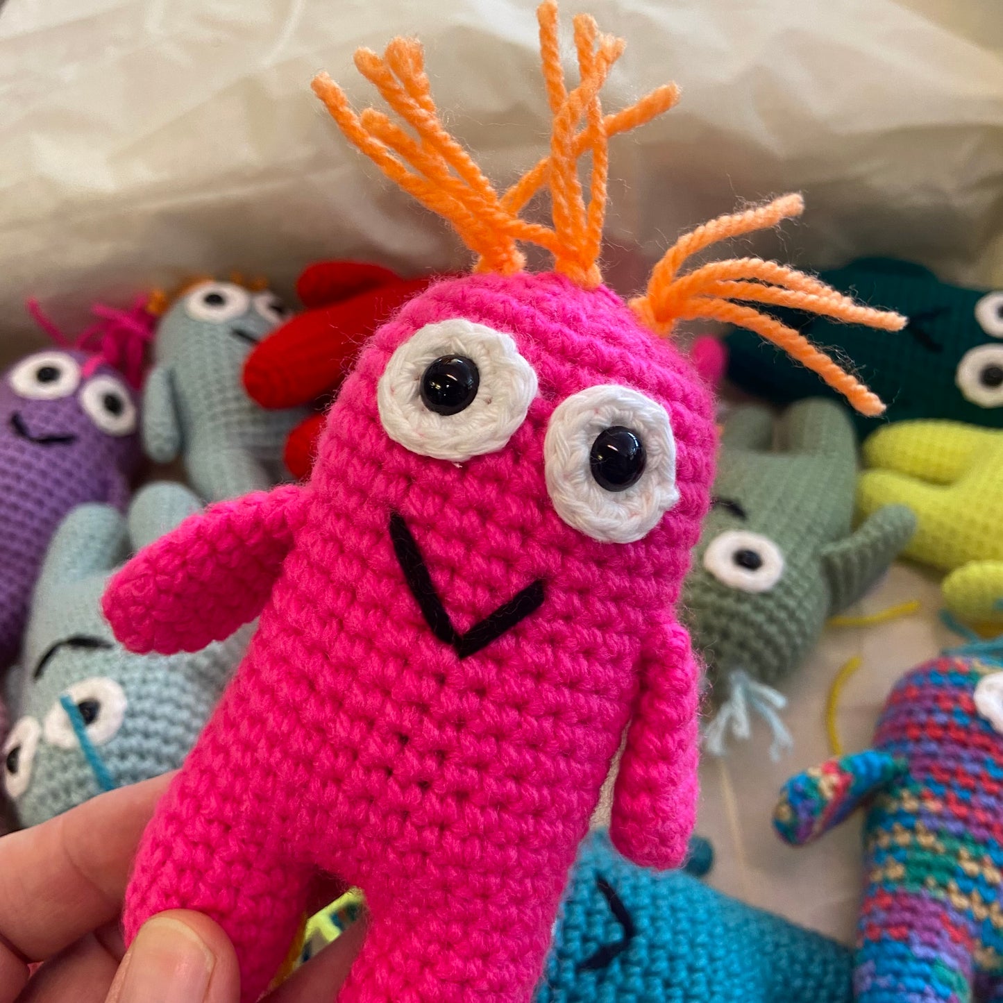 Pink crochet toy with orange antlers held in front of other colorful crochet toys.
