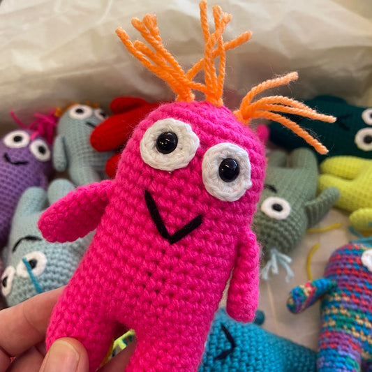 Pink crochet toy with orange antlers held in front of other colorful crochet toys.