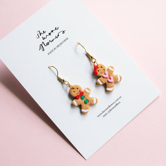 Gingerbread cookie-shaped earrings on a card with a pink background