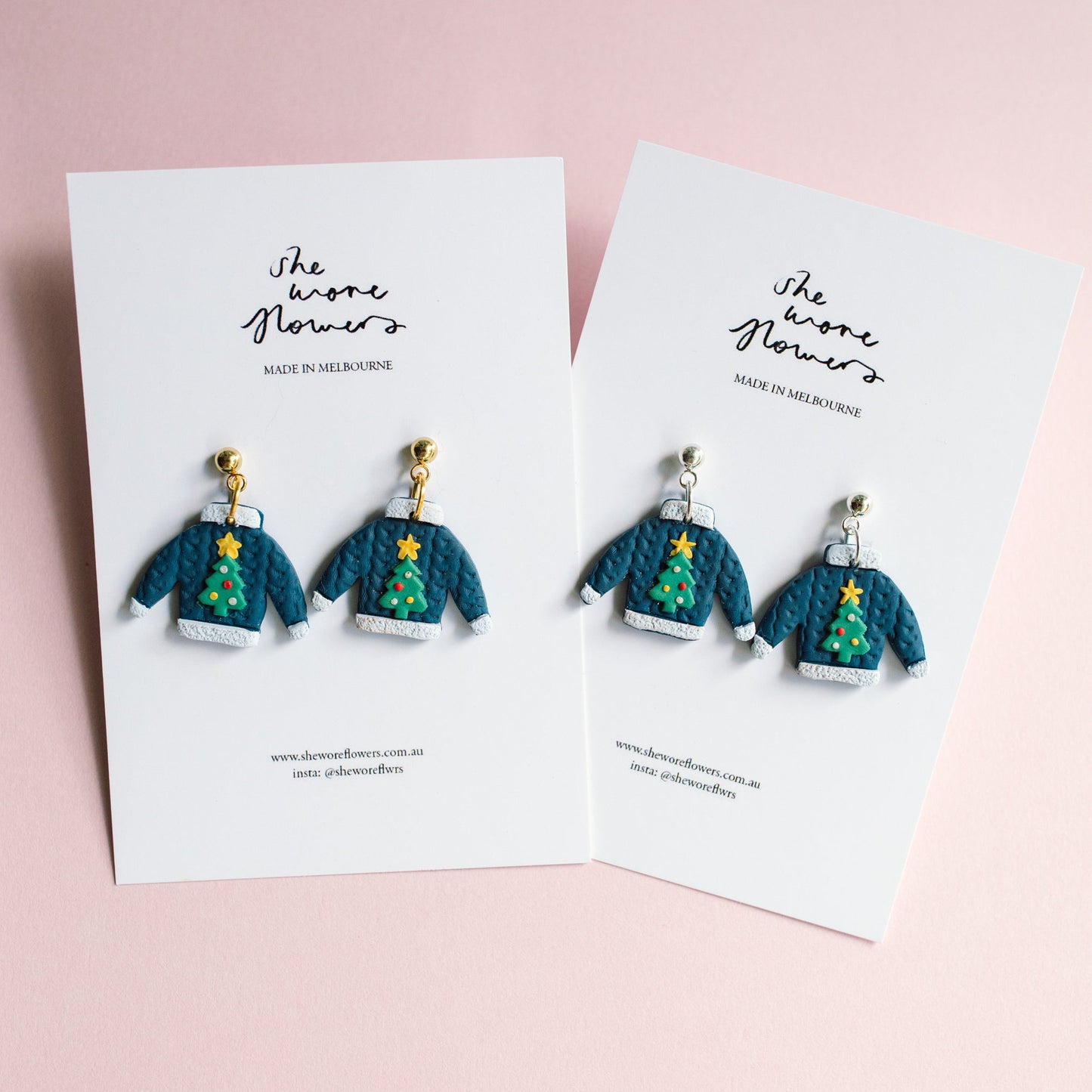 Pair of earrings resembling Christmas tree sweaters on branded cards against a pink background