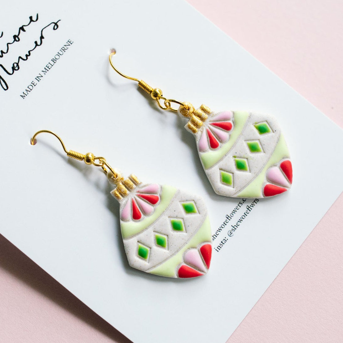 Decorative earrings on a card with a pink background