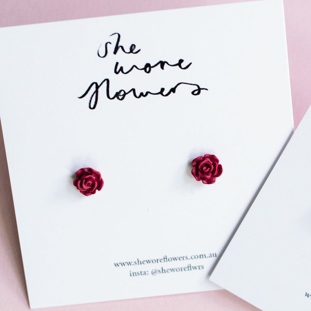 Red flower earrings on white cards with 'She wore flowers' text on a pink background
