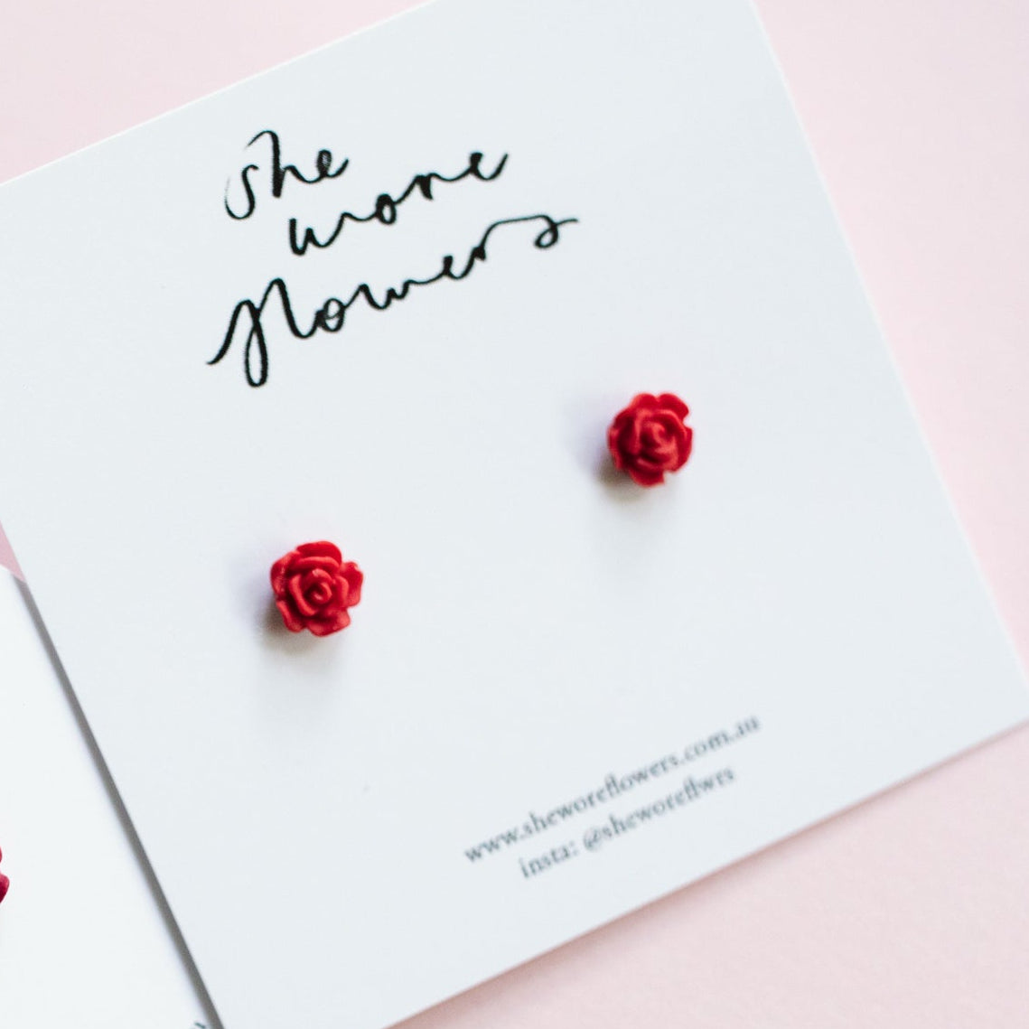 Red rose earrings on a card with 'She Wore Flowers' branding.
