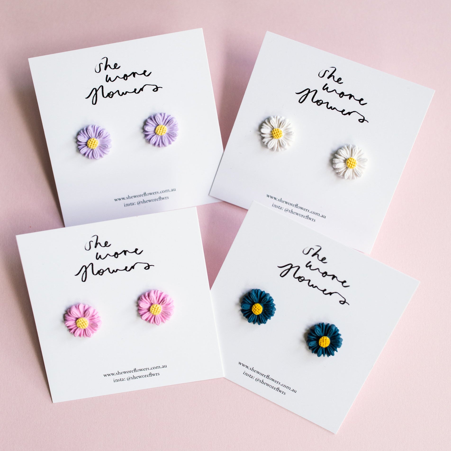 Set of floral earrings on branded cards against a pink background