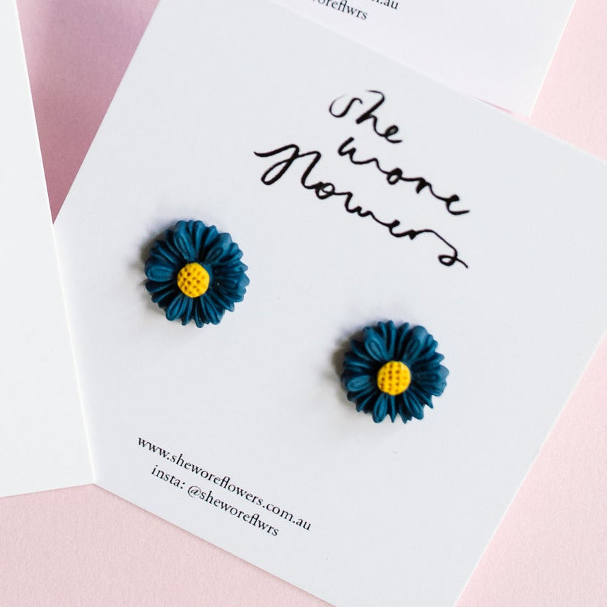 Set of floral earrings on branded cards against a pink background