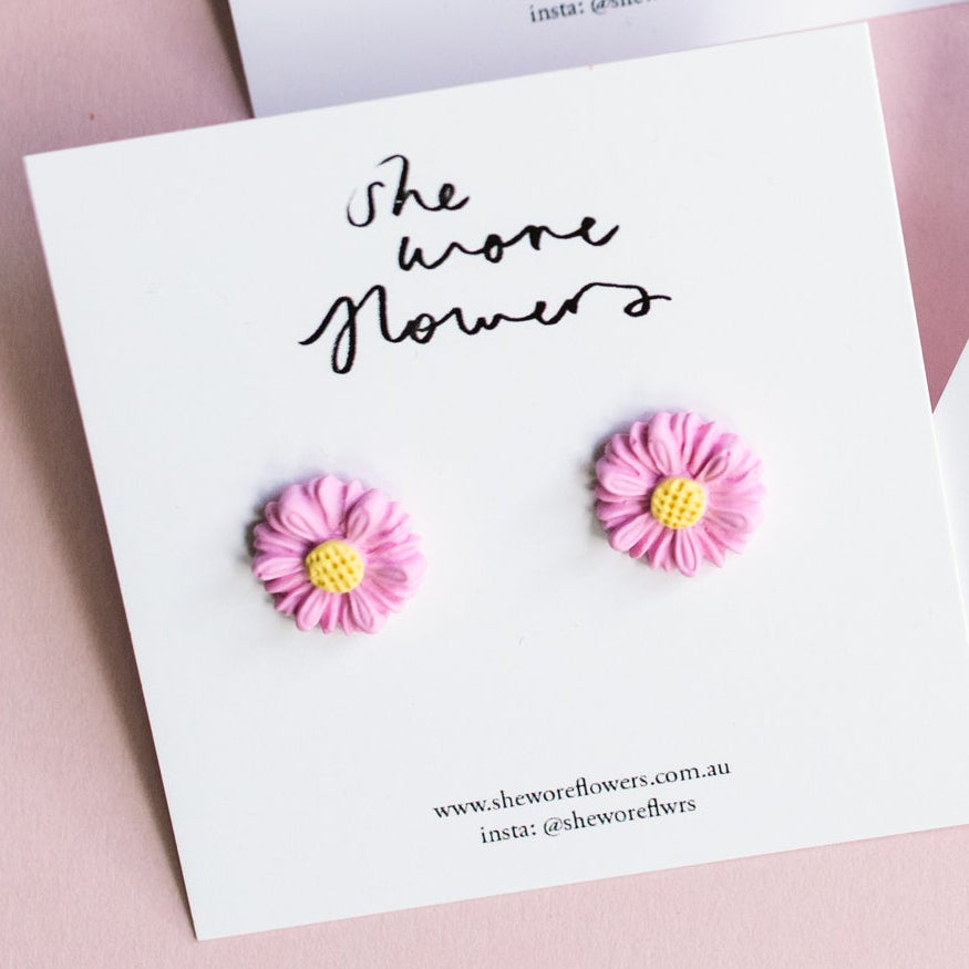 Set of floral earrings on branded cards against a pink background