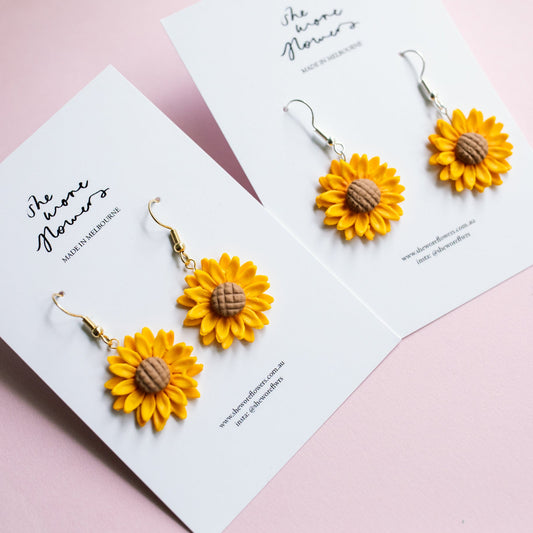 Yellow sunflower earrings on white cards with a pink background