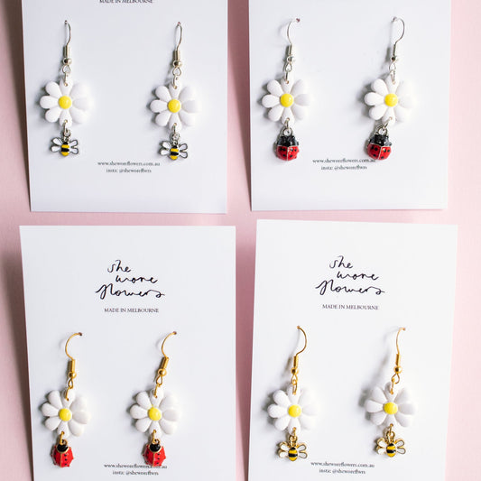 Set of floral earrings on branded cards against a pink background