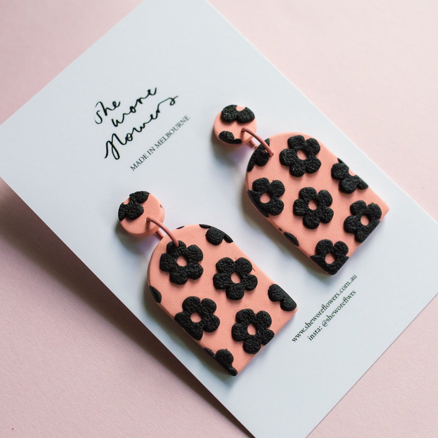 Pink earrings with black floral patterns on a light blue card with text