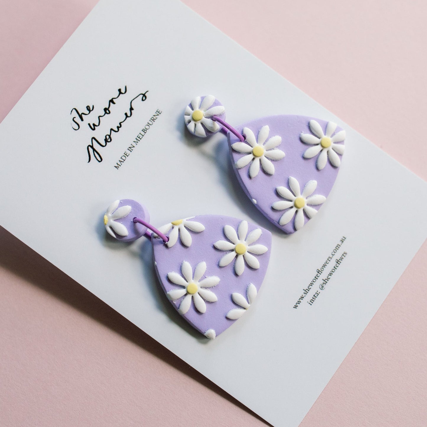 Heart-shaped earrings with floral designs on a white card against a pink background