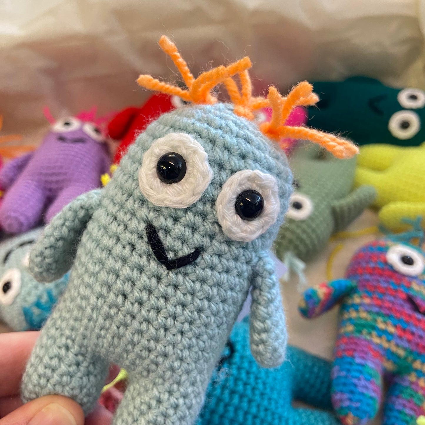 Crocheted toy with orange antennae held by a hand, surrounded by other colorful toys.