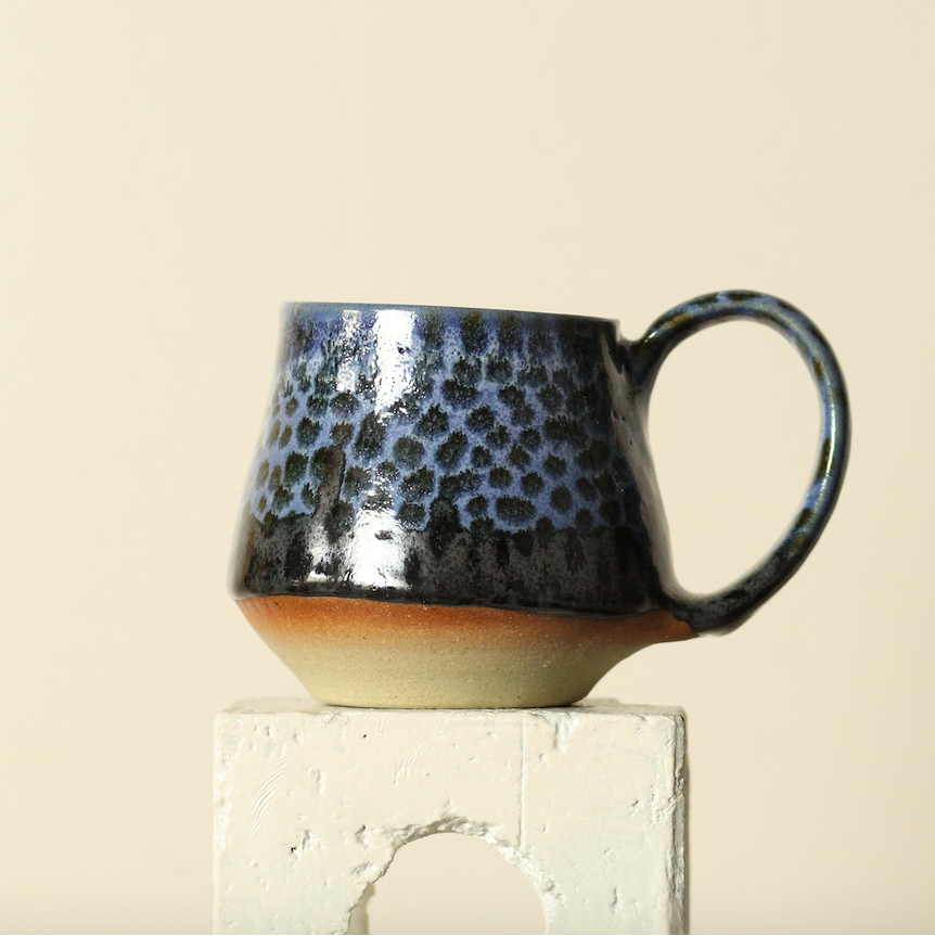 Ceramic mug with textured black exterior and beige interior on a light beige background