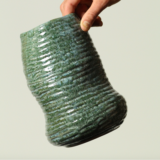 Hand holding a textured green ceramic vase against a neutral background