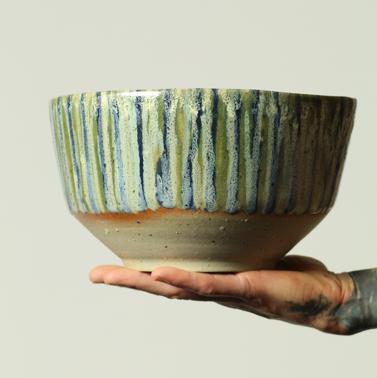 Hand holding a ceramic bowl with striped design on a plain background