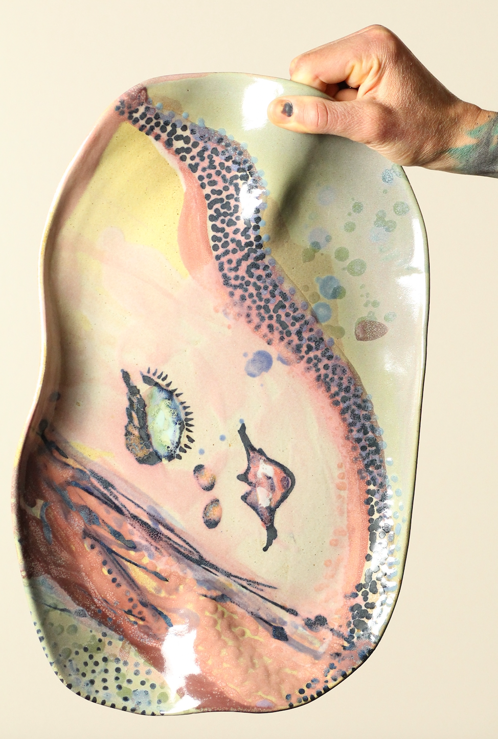 Hand holding a ceramic plate with artistic design on a beige background