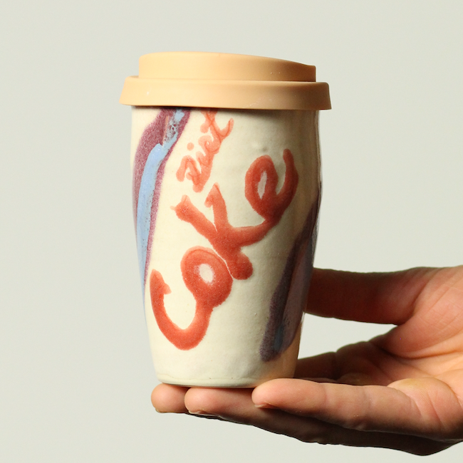 Hand holding a Coca-Cola cup with a beige lid against a light background