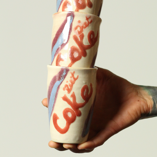 Stack of vintage-style 'Coke' cups held by a hand against a plain background
