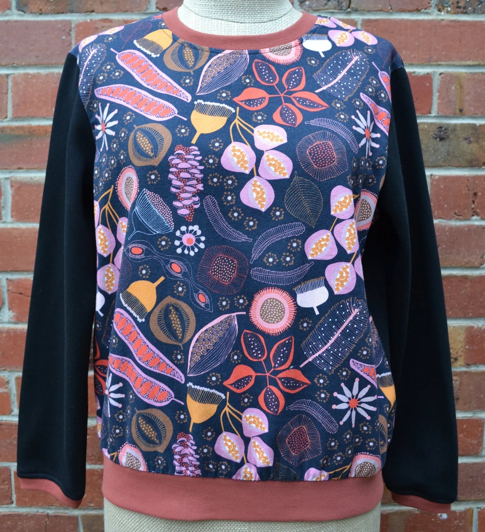 Floral patterned sweater on a mannequin against a brick wall.