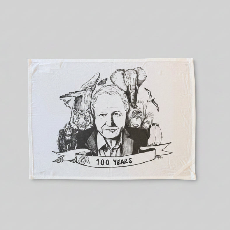 Tea towel with a black and white illustration of a person surrounded by animals and '100 Years' text on a wooden surface.